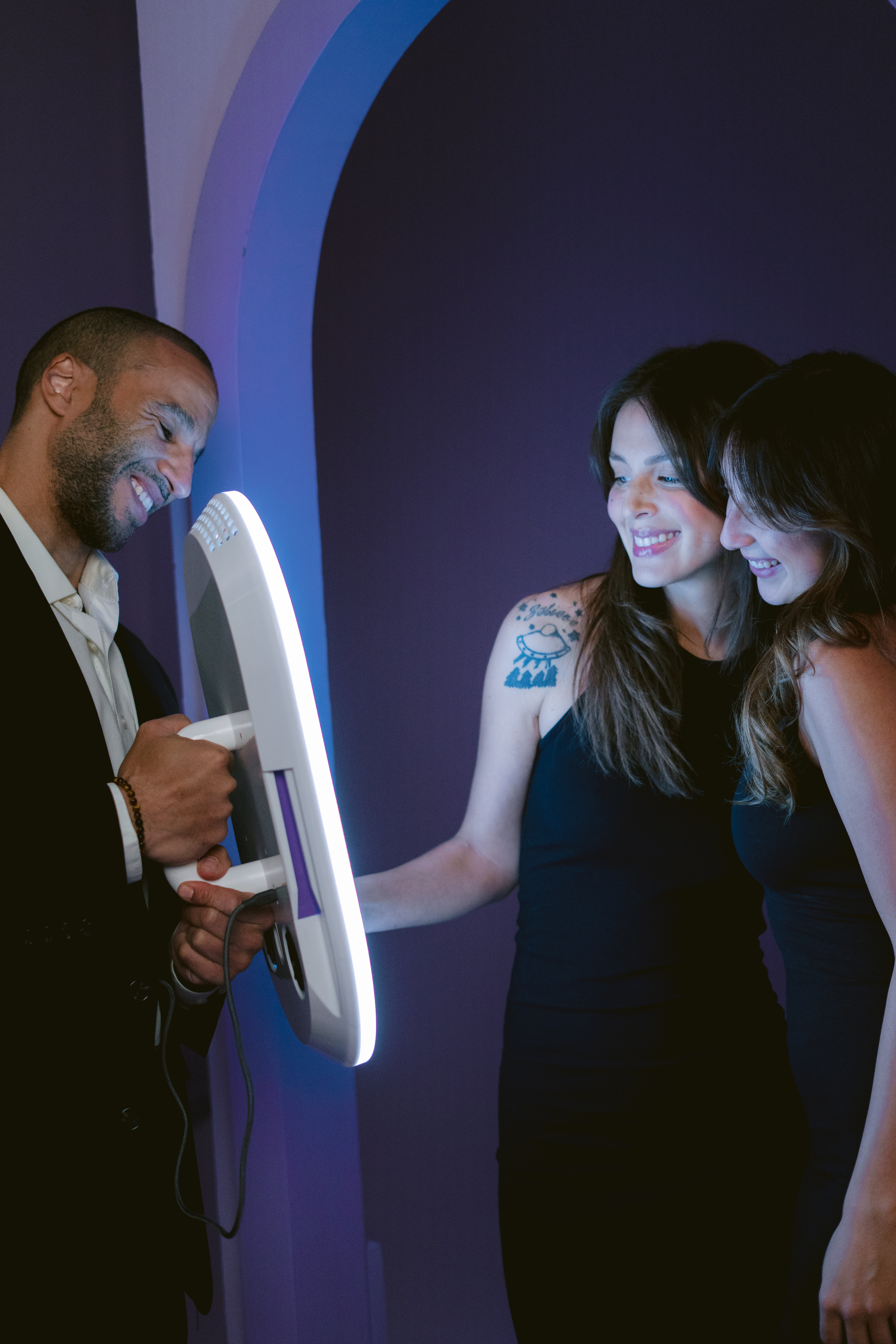 Guests using an illuminated Salsa 2 photo booth in colorful event lighting.